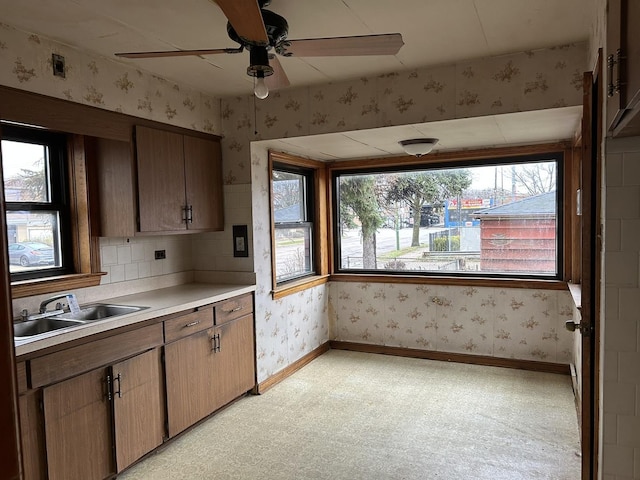 kitchen with a sink, baseboards, ceiling fan, and wallpapered walls