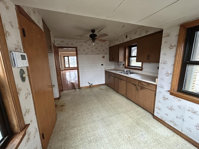 kitchen with a sink, light countertops, a ceiling fan, wallpapered walls, and light floors
