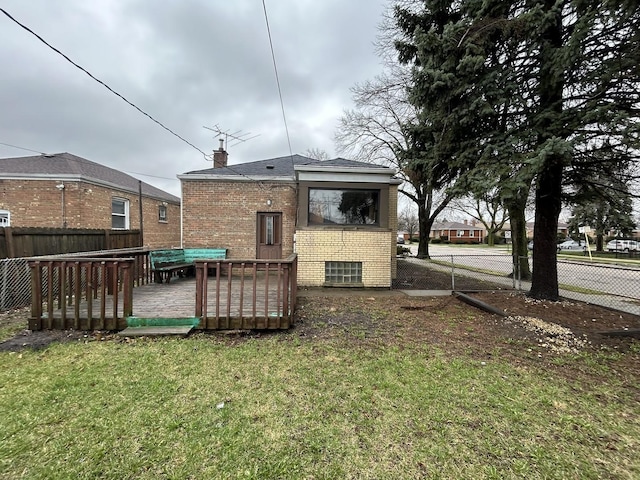 rear view of house with a chimney, brick siding, a fenced backyard, a wooden deck, and a yard