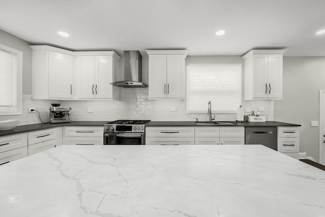 kitchen with a sink, wall chimney range hood, dishwashing machine, white cabinetry, and stainless steel gas range oven