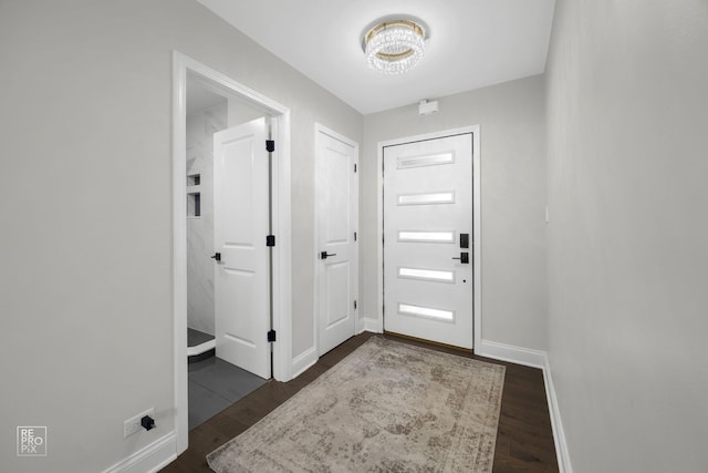 entrance foyer with dark wood-type flooring, an inviting chandelier, and baseboards