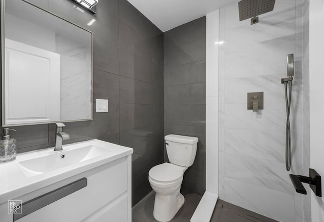 bathroom featuring toilet, vanity, a tile shower, and tile walls