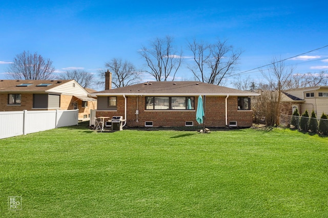 back of property featuring roof with shingles, a chimney, brick siding, a fenced backyard, and a lawn
