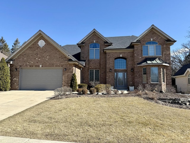 traditional-style home with roof with shingles, a front yard, brick siding, an attached garage, and driveway