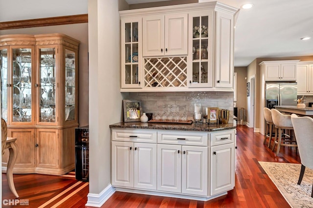 bar with dark wood-style flooring, backsplash, and stainless steel fridge