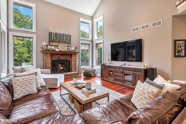 living room featuring high vaulted ceiling, visible vents, wood finished floors, and a healthy amount of sunlight