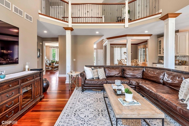 living area with a towering ceiling, visible vents, ornate columns, and wood finished floors
