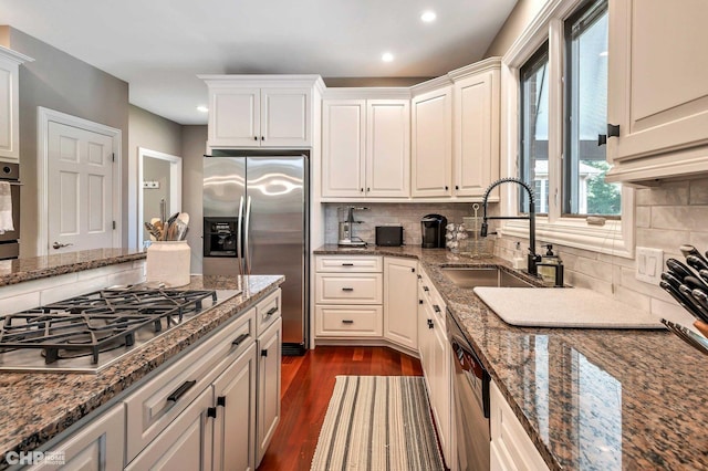 kitchen featuring a sink, backsplash, appliances with stainless steel finishes, and dark wood-style flooring