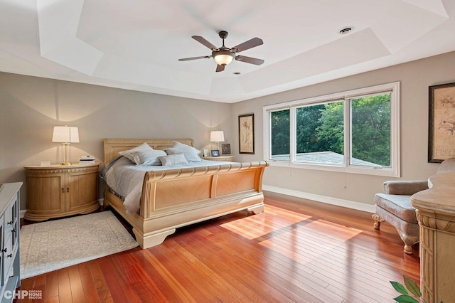 bedroom featuring baseboards, visible vents, a tray ceiling, ceiling fan, and light wood finished floors