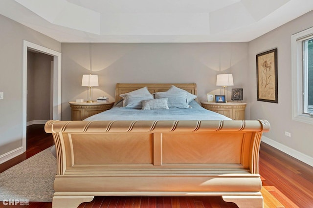 bedroom featuring a tray ceiling, wood finished floors, and baseboards