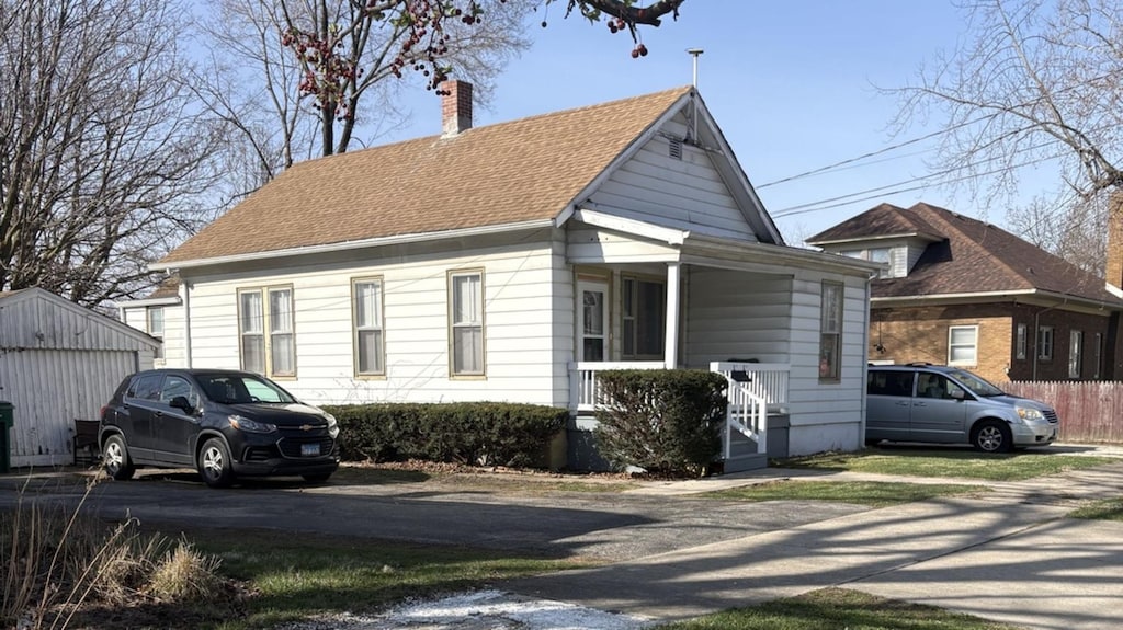 view of front of home with roof with shingles, an outdoor structure, a chimney, and covered porch