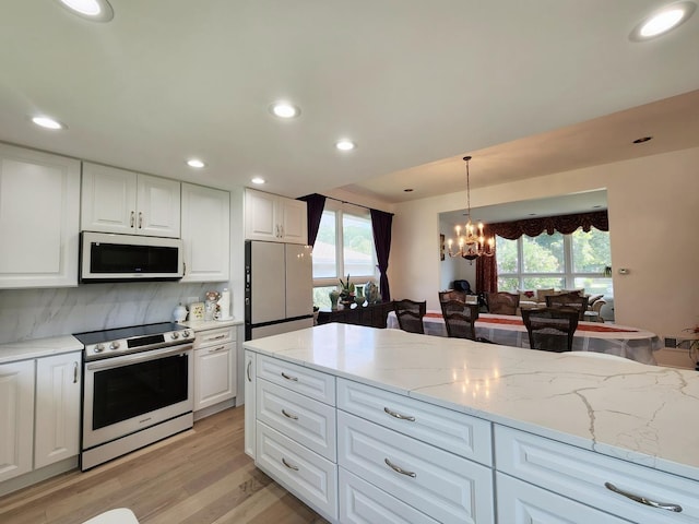 kitchen with white microwave, freestanding refrigerator, electric range, decorative backsplash, and a notable chandelier