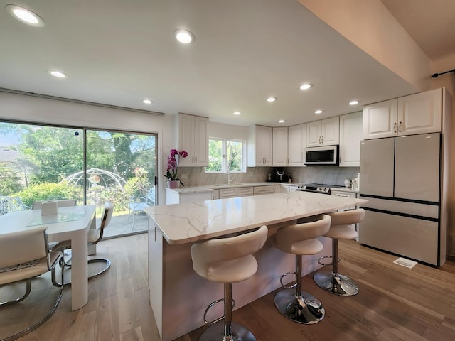 kitchen featuring light wood-style flooring, backsplash, light stone countertops, and stainless steel appliances