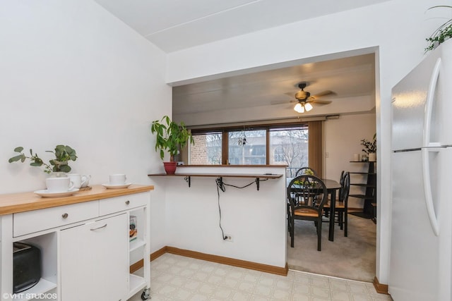 kitchen with baseboards, freestanding refrigerator, white cabinetry, a ceiling fan, and light floors