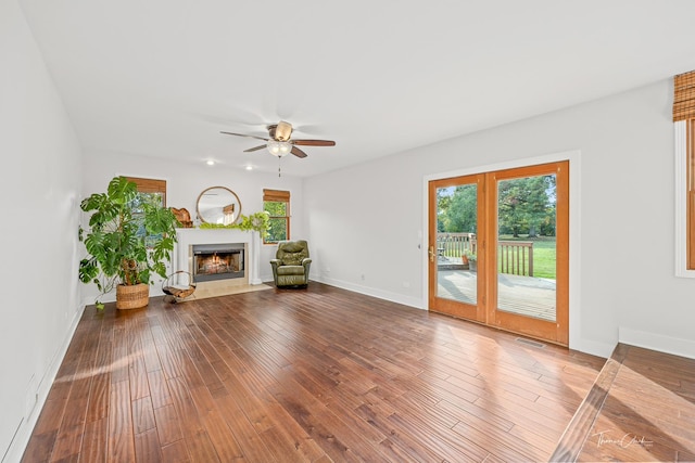 unfurnished living room with ceiling fan, hardwood / wood-style flooring, a premium fireplace, and baseboards