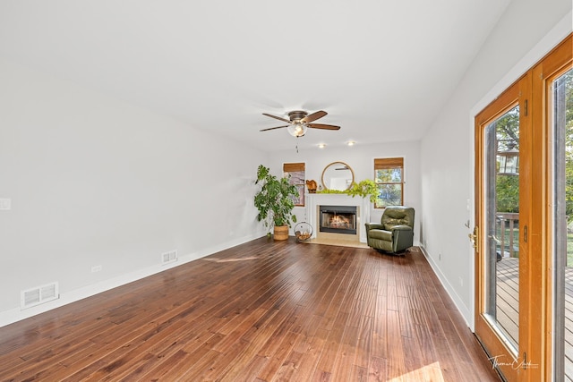 living area featuring visible vents, a ceiling fan, a warm lit fireplace, and dark wood-style floors