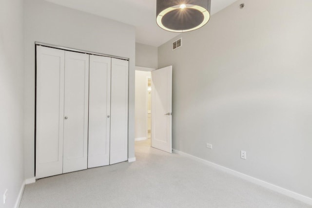 unfurnished bedroom with light carpet, visible vents, baseboards, and a closet