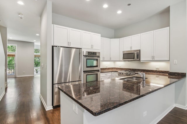 kitchen featuring dark stone counters, a peninsula, appliances with stainless steel finishes, and a sink
