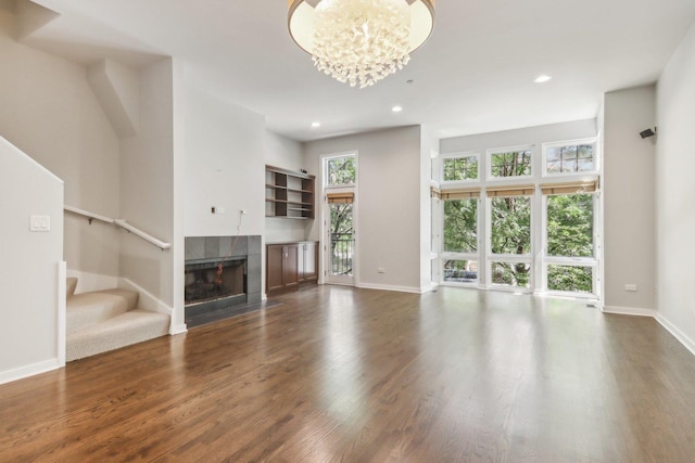 unfurnished living room with a tiled fireplace, dark wood-type flooring, and a notable chandelier
