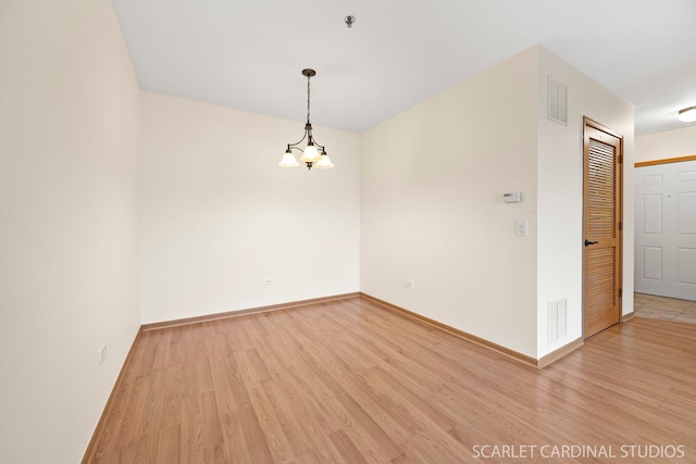 unfurnished room featuring an inviting chandelier, light wood finished floors, baseboards, and visible vents