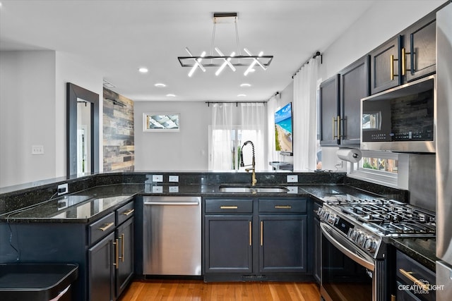 kitchen featuring dark stone countertops, a notable chandelier, a sink, stainless steel appliances, and light wood-style flooring