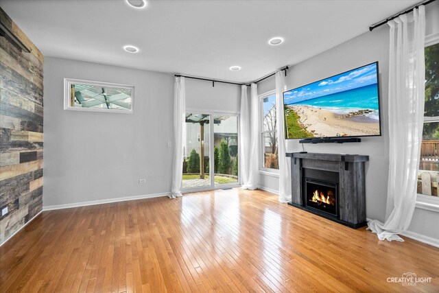 unfurnished living room with baseboards, a warm lit fireplace, and hardwood / wood-style flooring