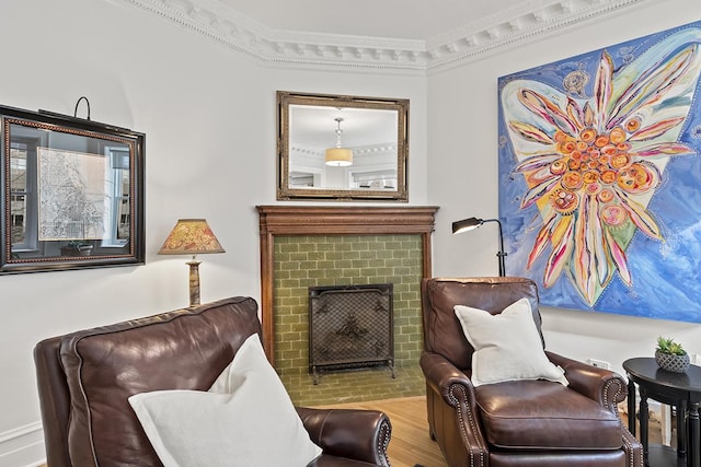 sitting room with a brick fireplace, wood finished floors, and ornamental molding
