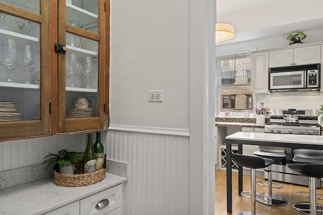 bar area with appliances with stainless steel finishes, wainscoting, and light wood-style floors