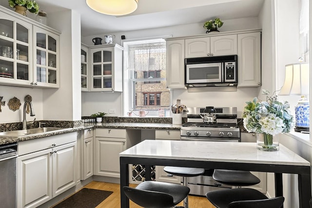 kitchen featuring appliances with stainless steel finishes, a sink, glass insert cabinets, and dark stone counters