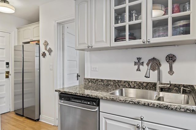 kitchen featuring appliances with stainless steel finishes, a sink, light wood-style flooring, glass insert cabinets, and dark stone counters