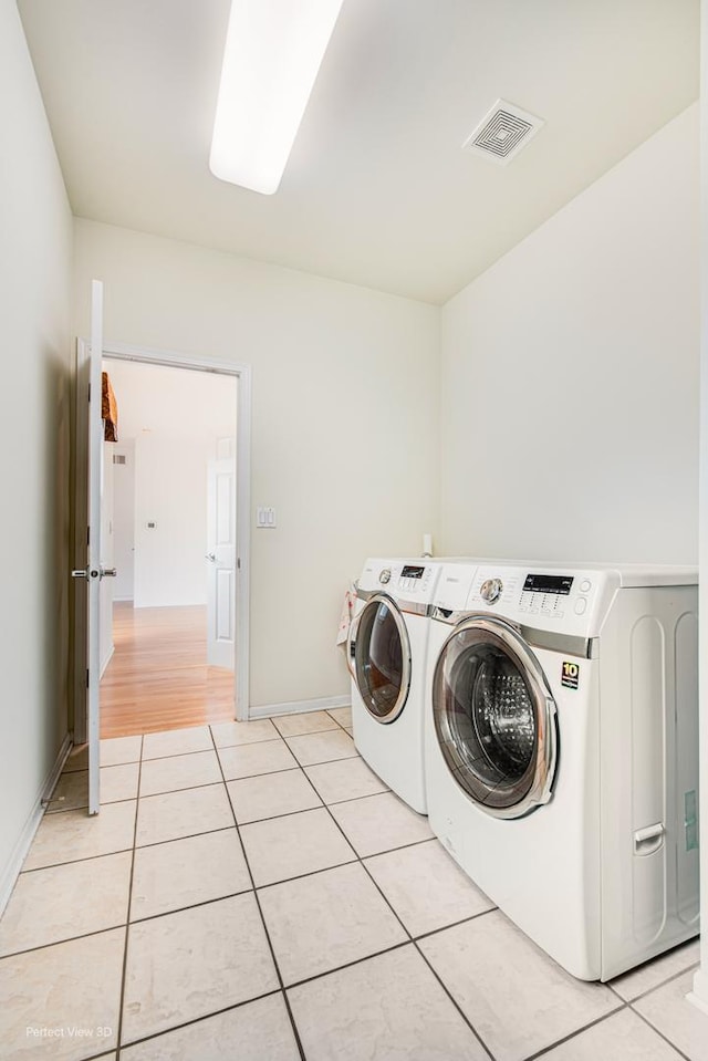 clothes washing area with baseboards, light tile patterned floors, washing machine and dryer, visible vents, and laundry area