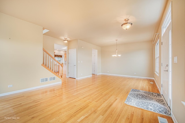 interior space featuring baseboards, an inviting chandelier, light wood-style flooring, stairs, and visible vents