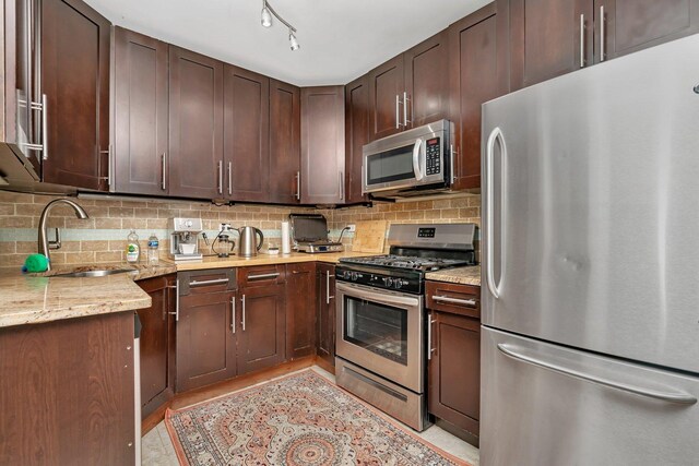 kitchen featuring tasteful backsplash, a sink, appliances with stainless steel finishes, dark brown cabinets, and light stone counters