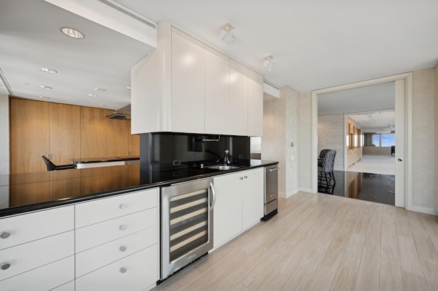 kitchen with dark countertops, white cabinets, stainless steel dishwasher, light wood finished floors, and beverage cooler