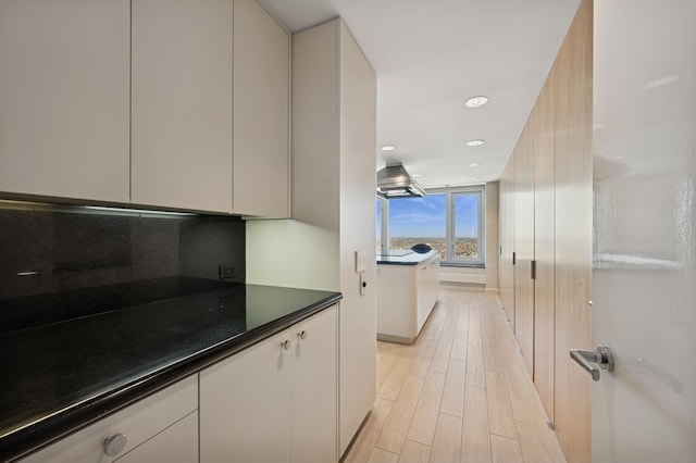 kitchen featuring island exhaust hood, recessed lighting, backsplash, dark countertops, and light wood finished floors