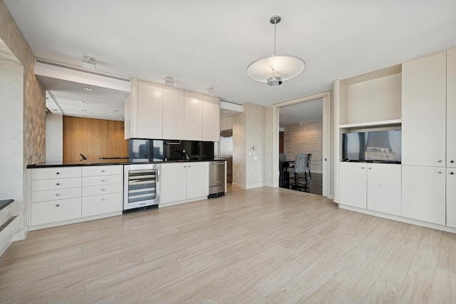 kitchen with wine cooler, white cabinets, dark countertops, and light wood-style flooring