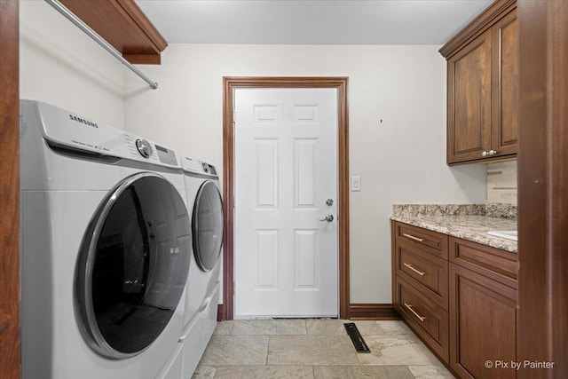 clothes washing area with stone finish flooring, baseboards, washing machine and clothes dryer, and cabinet space
