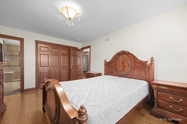 bedroom with a closet, wood finished floors, baseboards, and visible vents