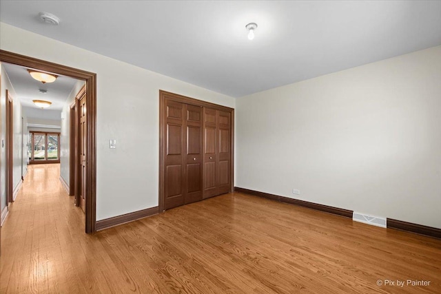 unfurnished bedroom featuring visible vents, light wood-style flooring, a closet, and baseboards