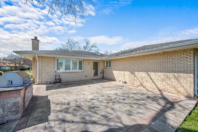 back of property featuring a patio area, brick siding, area for grilling, and a chimney