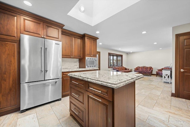 kitchen with light stone countertops, a kitchen island, recessed lighting, backsplash, and high end fridge