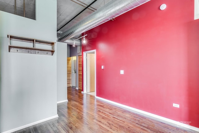 empty room featuring baseboards, wood finished floors, and a high ceiling