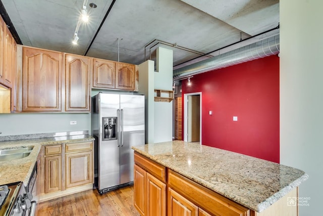 kitchen with appliances with stainless steel finishes, light stone counters, a sink, light wood finished floors, and a center island