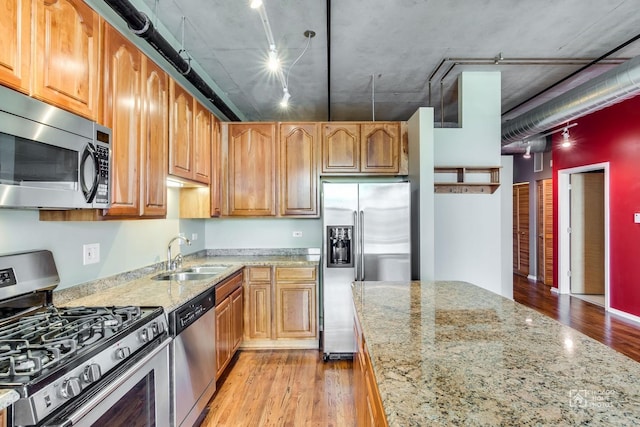 kitchen featuring appliances with stainless steel finishes, light stone countertops, rail lighting, a sink, and light wood finished floors