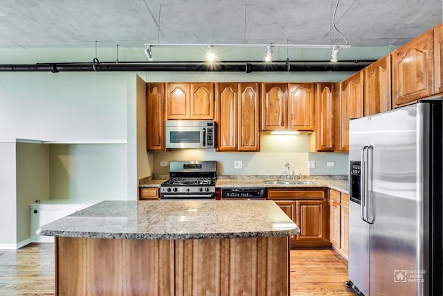 kitchen with a kitchen island, rail lighting, a sink, light wood finished floors, and stainless steel appliances