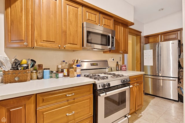 kitchen featuring light countertops, light tile patterned floors, brown cabinetry, and stainless steel appliances