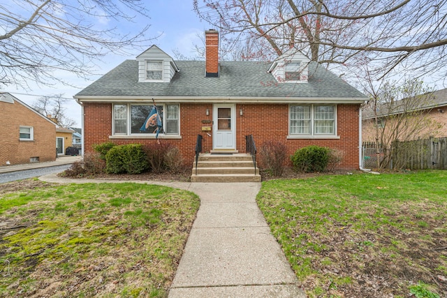 new england style home with brick siding, a front yard, roof with shingles, and fence