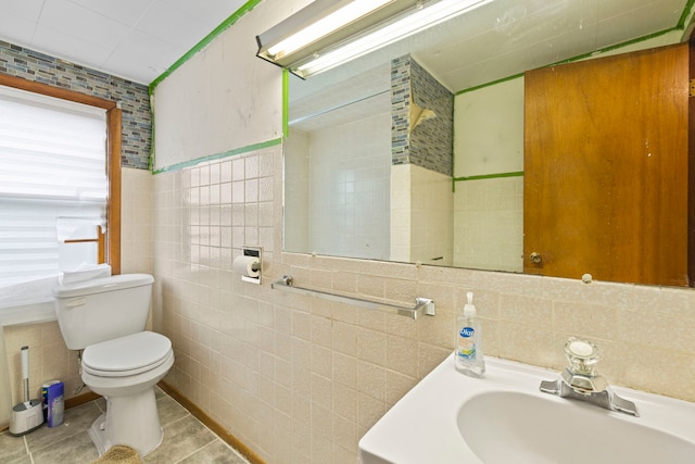 bathroom with toilet, tile patterned floors, a sink, and tile walls