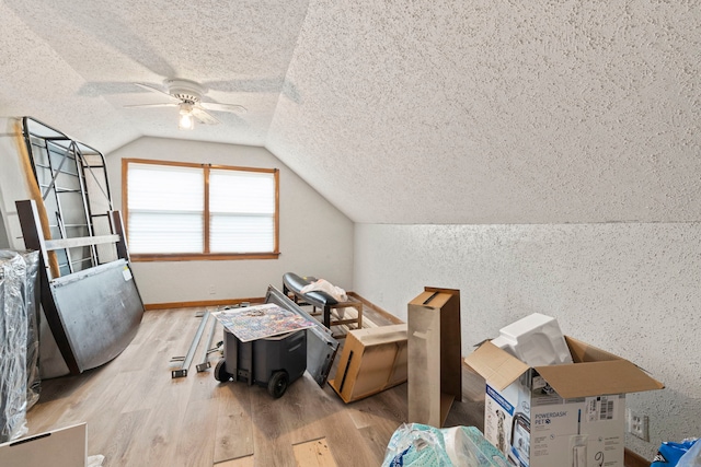 additional living space with vaulted ceiling, a textured wall, light wood-style flooring, a textured ceiling, and a ceiling fan