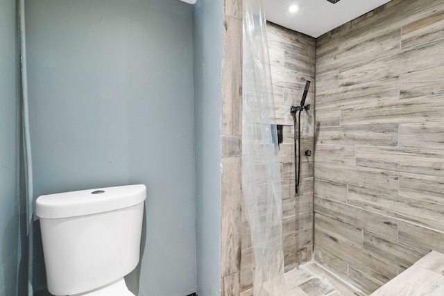 full bathroom featuring tiled shower and toilet